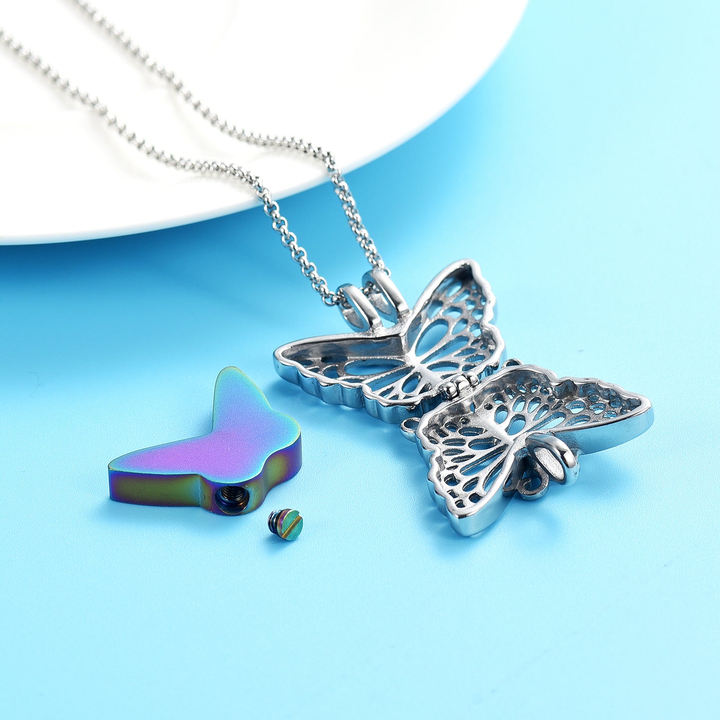 Disassembled Butterfly Urn Pendant Rainbow showing internal ash compartment and screw cap, crafted from stainless steel with rainbow insert.